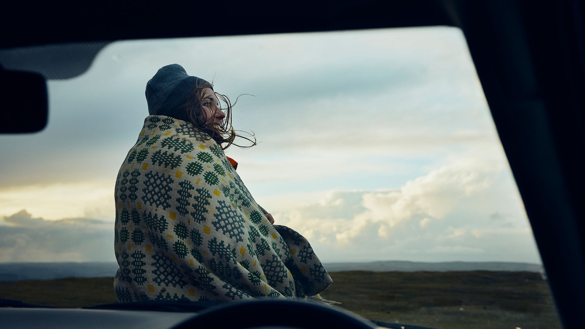 Person wrapped up warm sitting on car bonnet